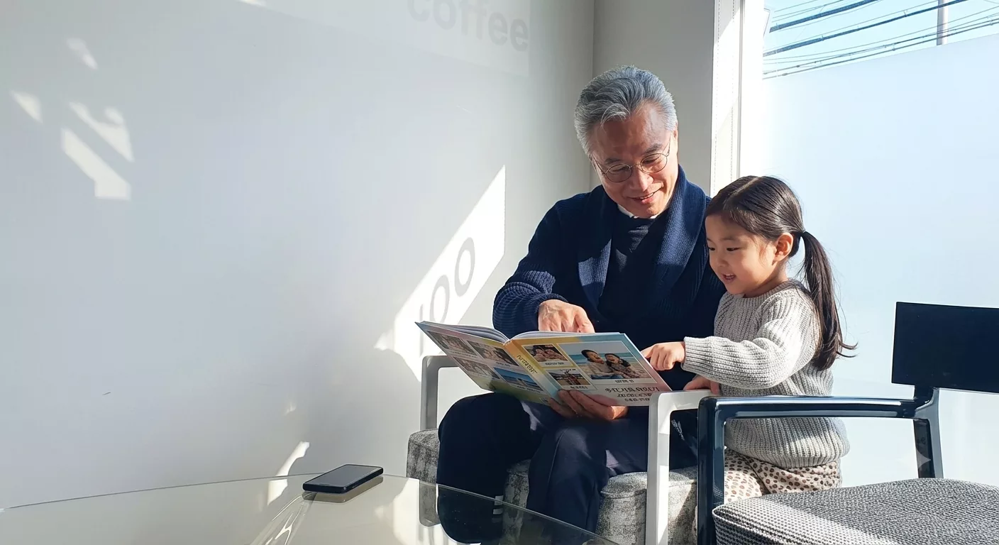 햇살이 드는 카페에서 할아버지와 손녀가 함께 포토북을 펼쳐 보며 웃는 모습